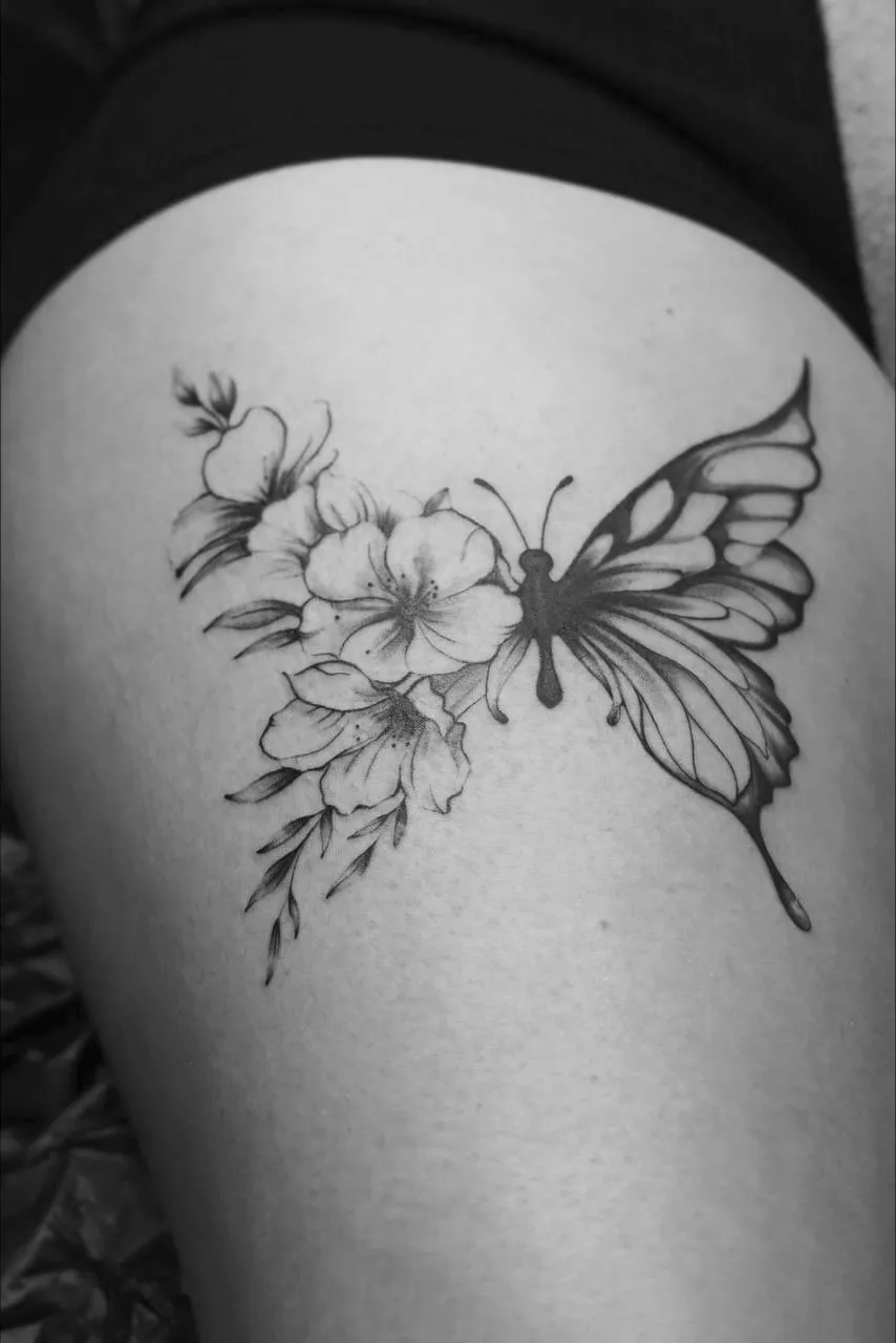Fine line butterfly and floral thigh tattoo with soft black and grey shading and delicate botanical details.