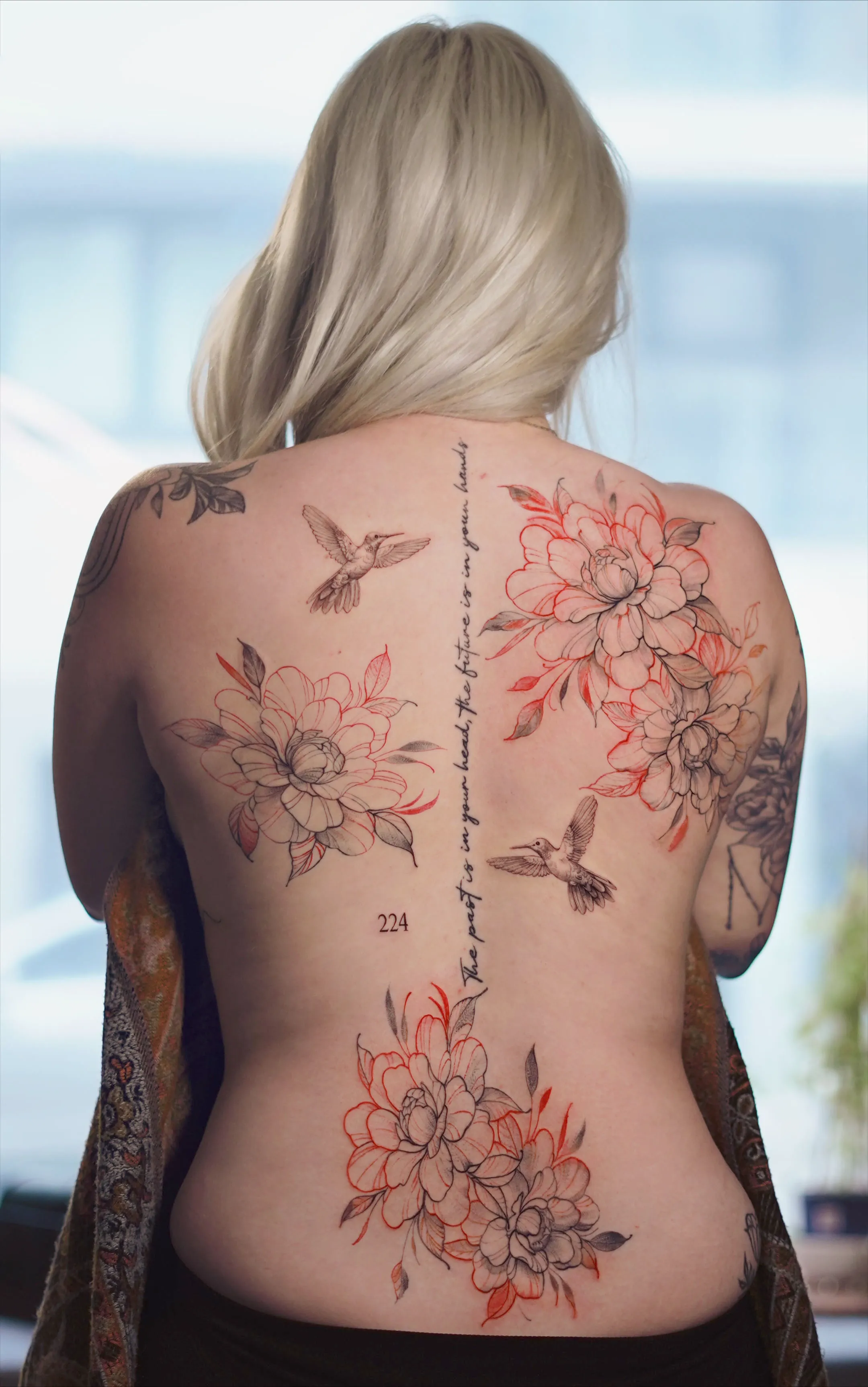 Fine line floral back piece tattoo with peonies, hummingbirds, and script lettering along the spine.