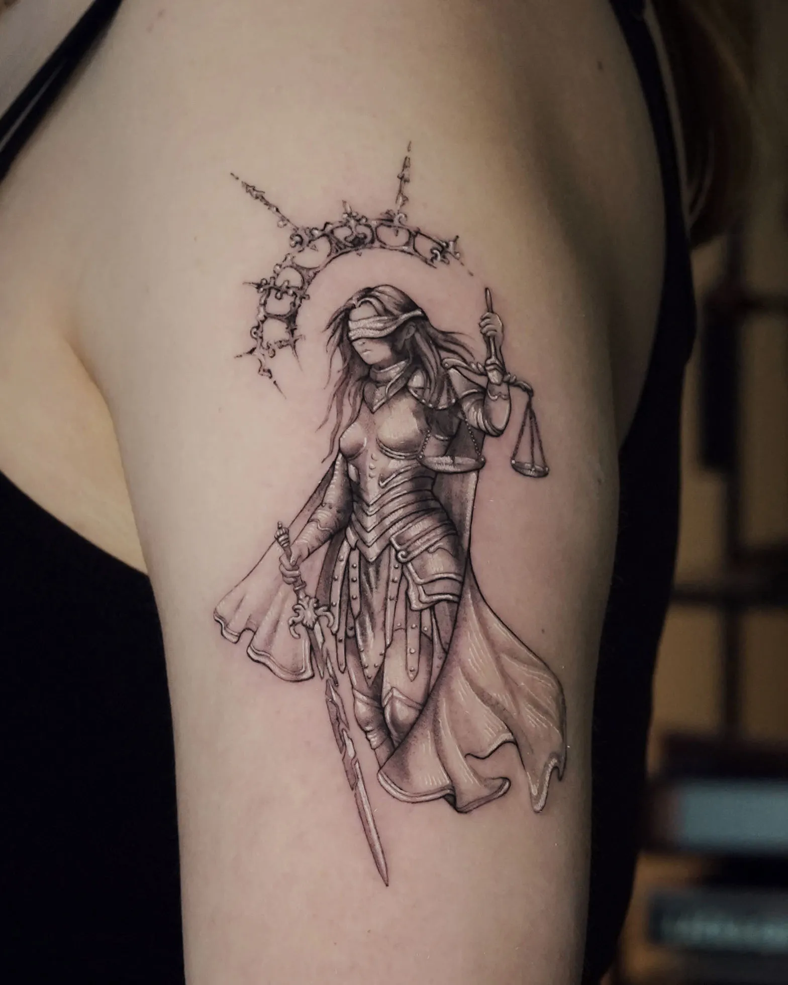 Fine line black and grey Lady Justice tattoo on the upper arm with delicate shading and detailed linework.