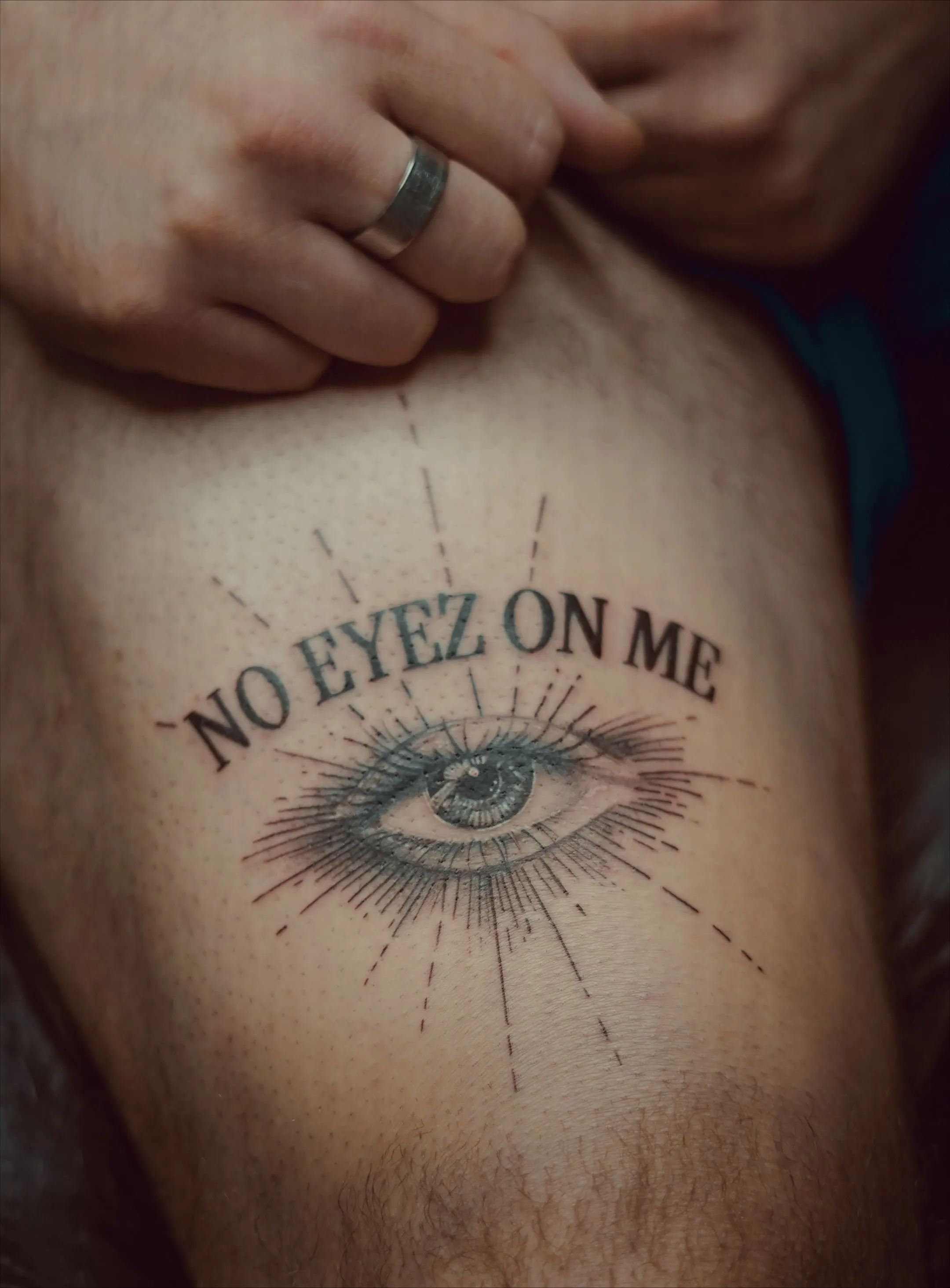 A tattoo of an eye and script above that says no eyez on me