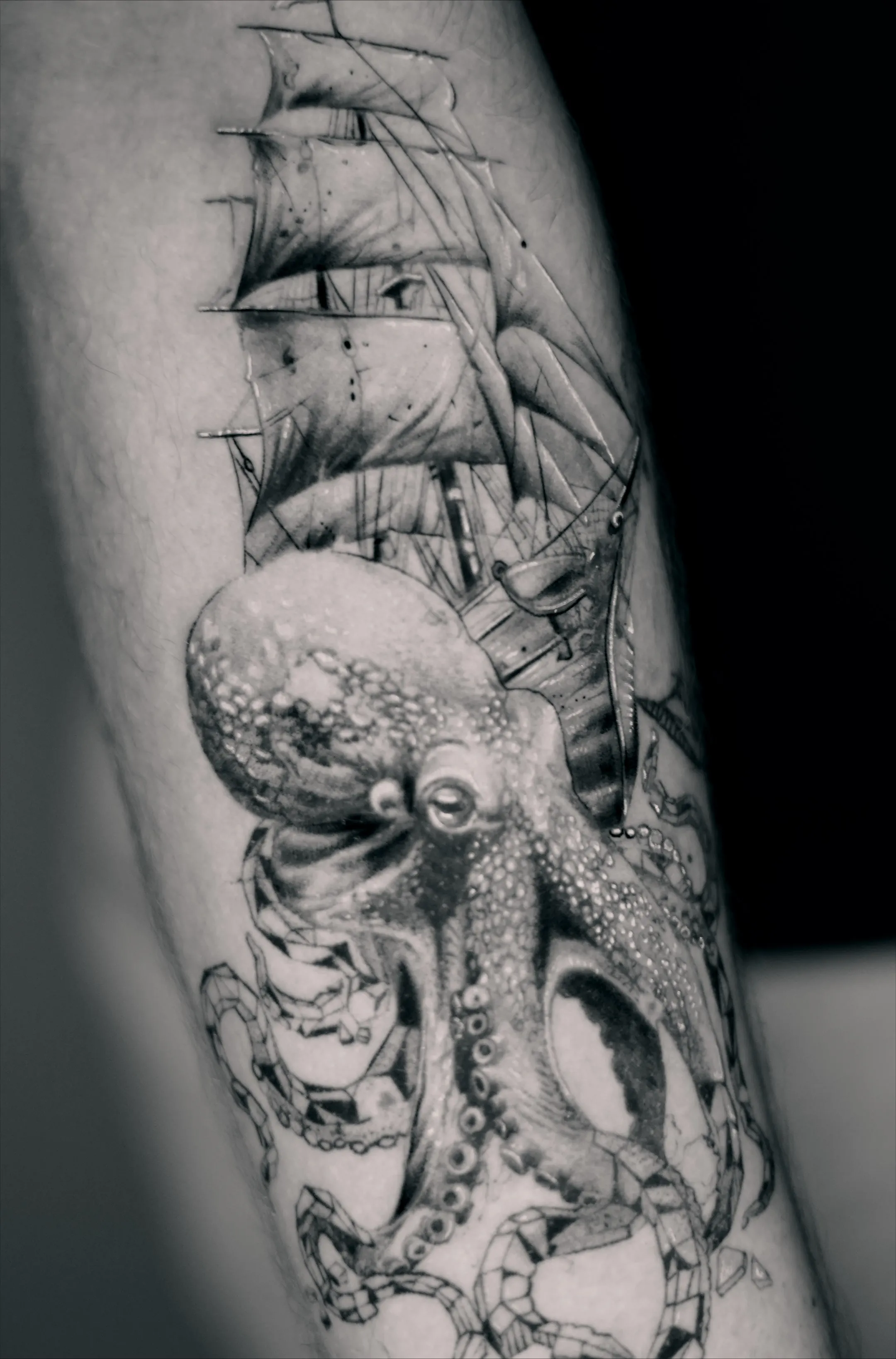 Realistic octopus and sailing ship tattoo with detailed black and grey shading and maritime imagery.